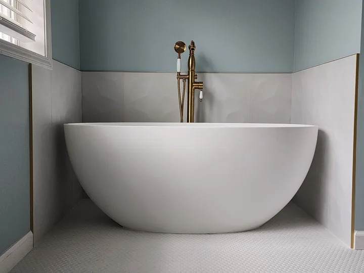 Freestanding white tub with large light wall tile, small white floor tile, and warm-metal fixtures