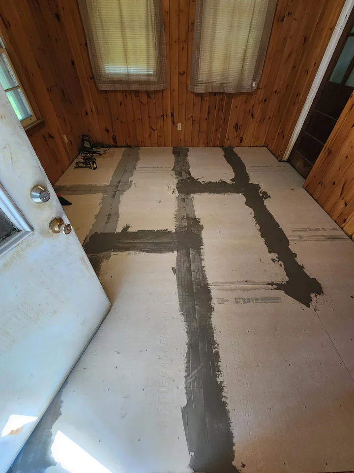 The same wood-paneled room with underlayment fitted across the floor before tile installation