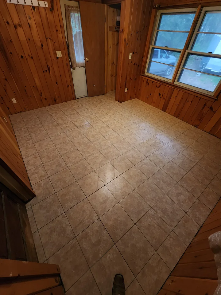 Light square-format tile floor in a compact room with wood-paneled walls, a doorway, and windows