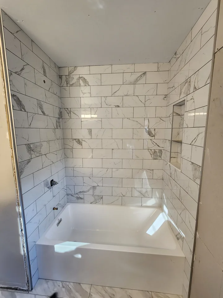 In-progress tub surround with marble-look rectangular tile across three walls and a built-in niche