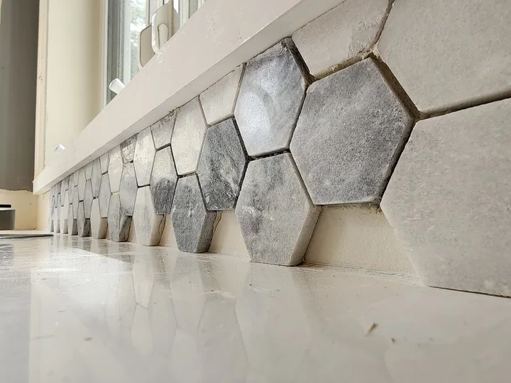 Close view of gray-and-white hex tile being laid beneath the kitchen window